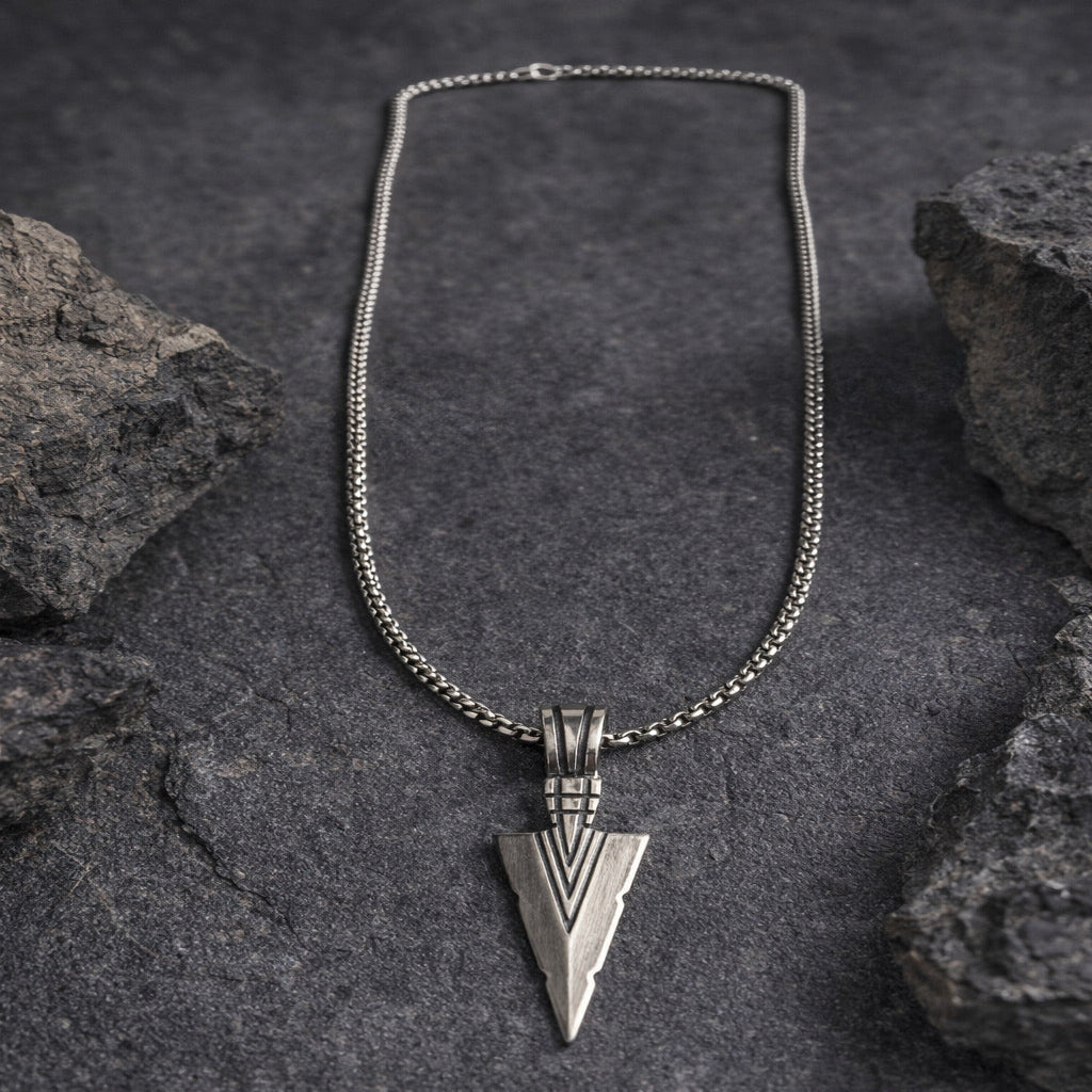 Silver necklace with an arrowhead pendant on a dark stone background