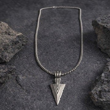 Silver necklace with an arrowhead pendant on a dark stone background