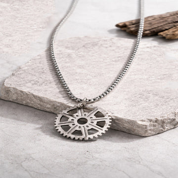 Silver gear-shaped pendant necklace on a stone surface