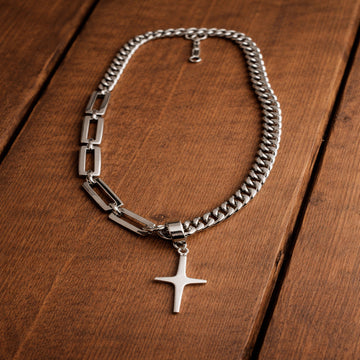 Silver chain necklace with a cross pendant on a wooden surface