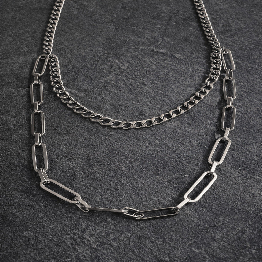 Two silver chain necklaces on a dark textured surface