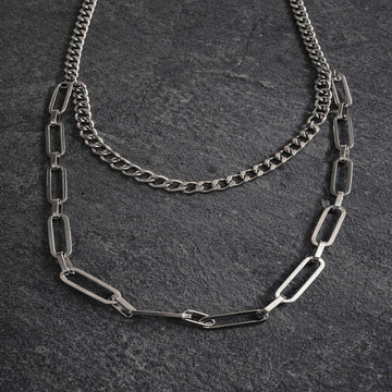 Two silver chain necklaces on a dark textured surface