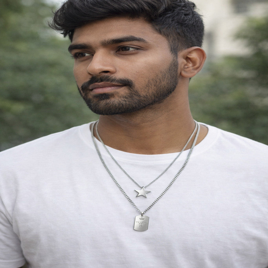Man wearing a white shirt with layered necklaces against a blurred green background