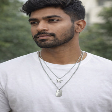 Man wearing a white shirt with layered necklaces against a blurred green background