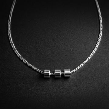 Silver necklace with three cylindrical pendants on a black background