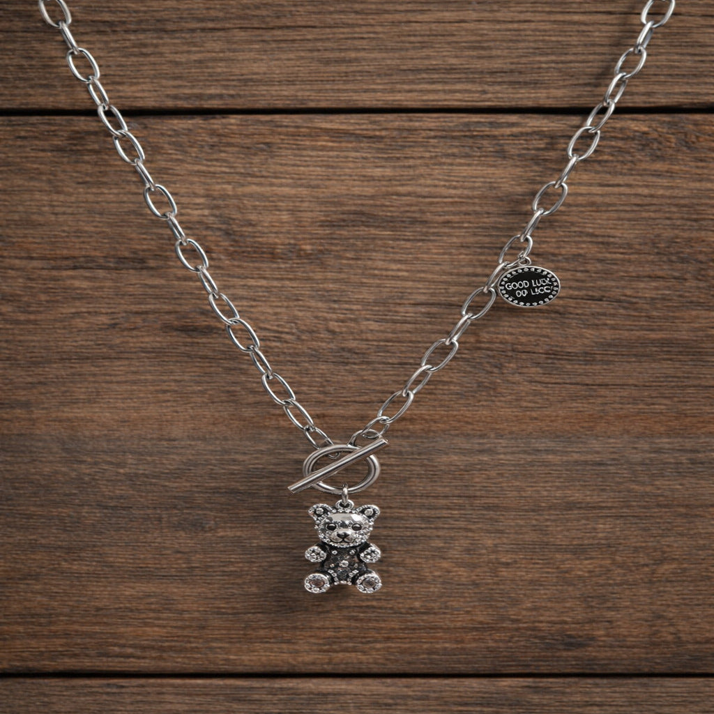 Silver necklace with a teddy bear pendant on a wooden surface