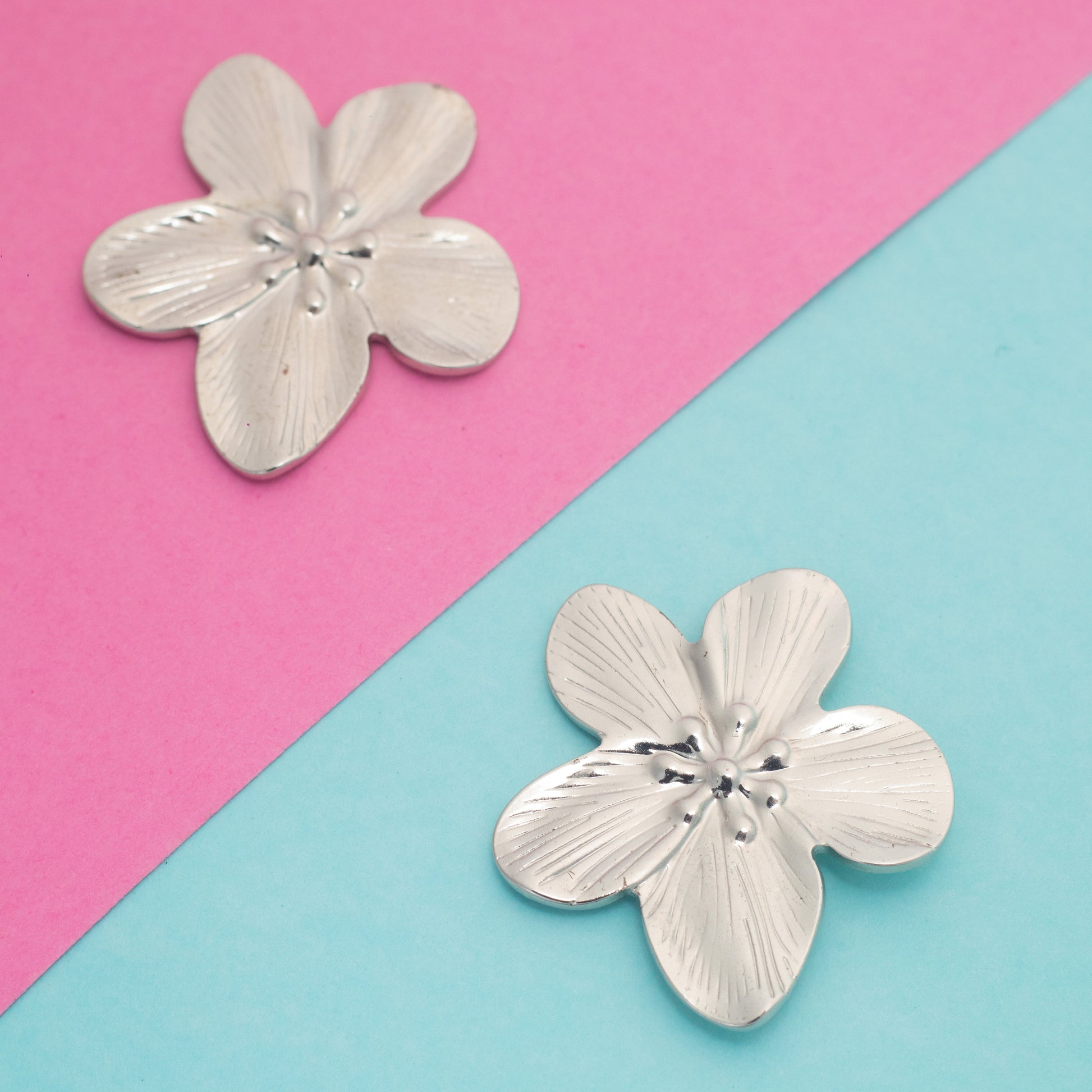 Silver flower-shaped earrings on a pink and blue background