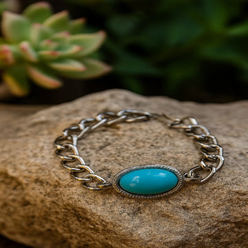 Silver chain bracelet with a turquoise stone on a rock with a succulent plant in the background