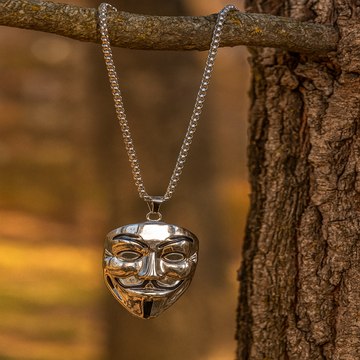 Silver mask pendant necklace hanging on a tree branch with a blurred natural background