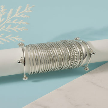 Stack of silver bracelets on a white surface with a light blue background