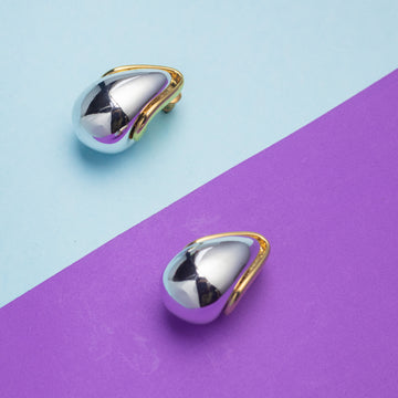 Two metallic teardrop-shaped earrings on a two-tone blue and purple background