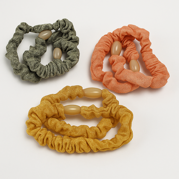 Three scrunchies in green, orange, and yellow with beige beads on a white background