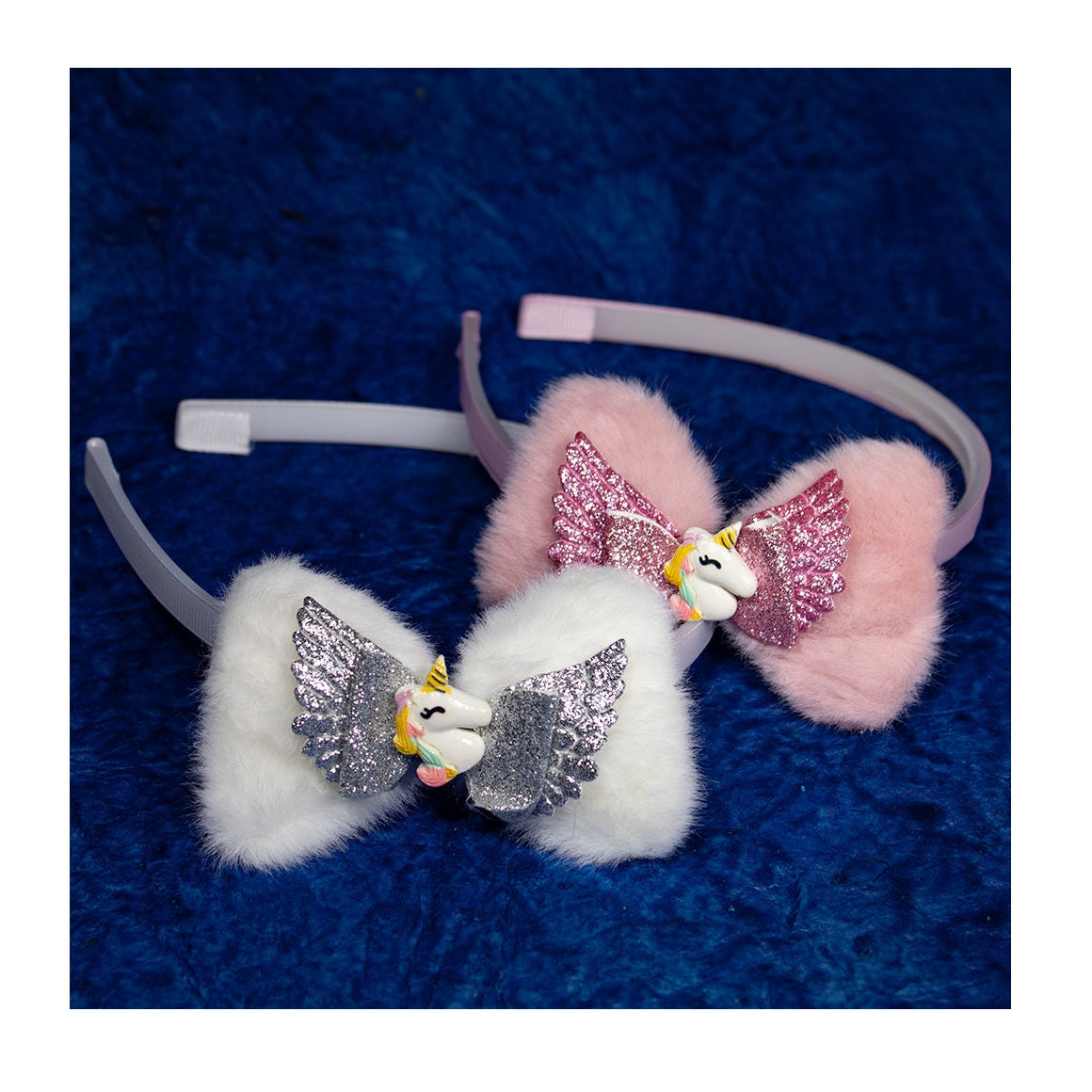 Two kids' hair bands with plush attachments, one in pink and one in white, with sparkly butterfly decorations, displayed on a blue textured surface.