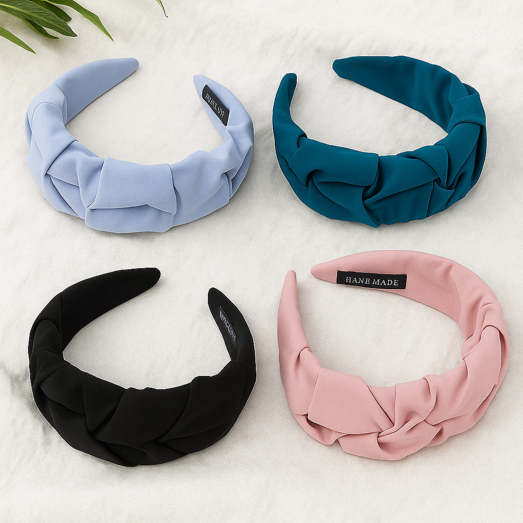 Four headbands in blue, black, pink, and green on a white surface with a leafy green plant.