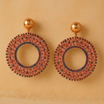 Gold earrings with circular design and gemstones on a beige background