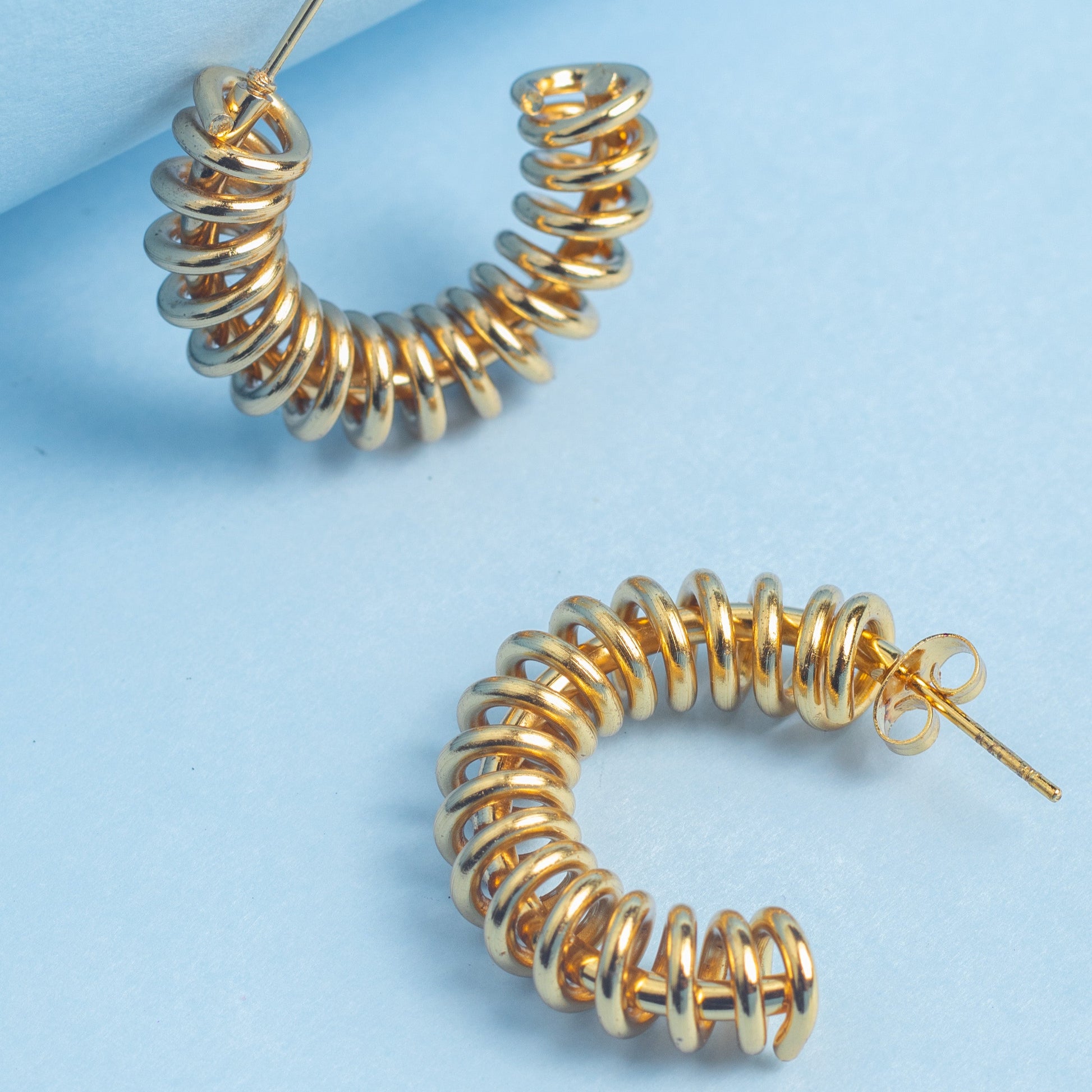 Gold spiral hoop earrings on a light blue background