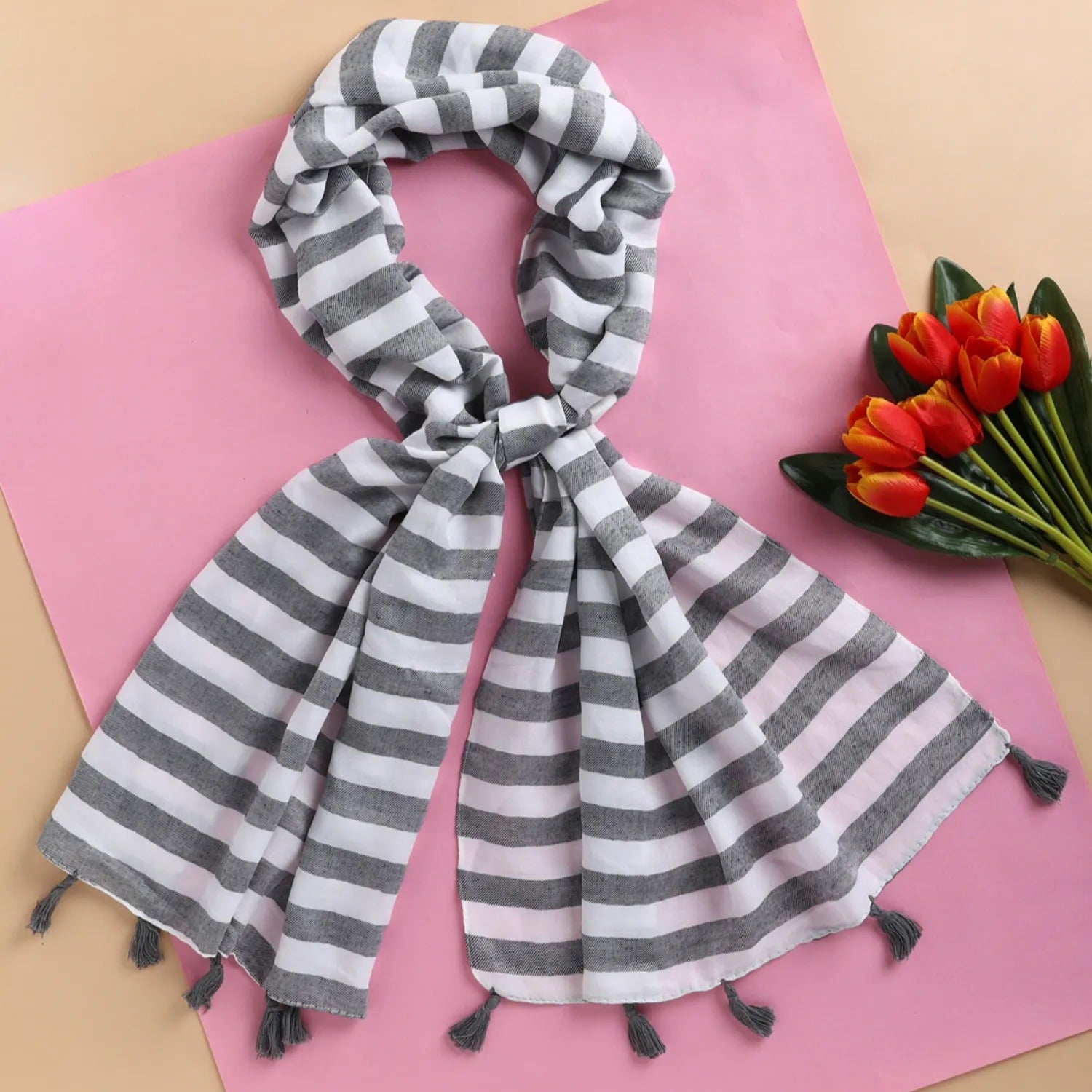 A gray and white striped viscose stole with embellishments spread out on a pink surface.