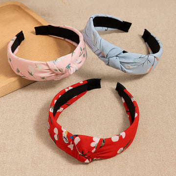Three floral-patterned headbands in pink, blue, and red on a beige surface.