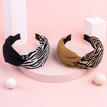 Two headbands, one black and white striped and one brown with black and white pattern, on a pink background.