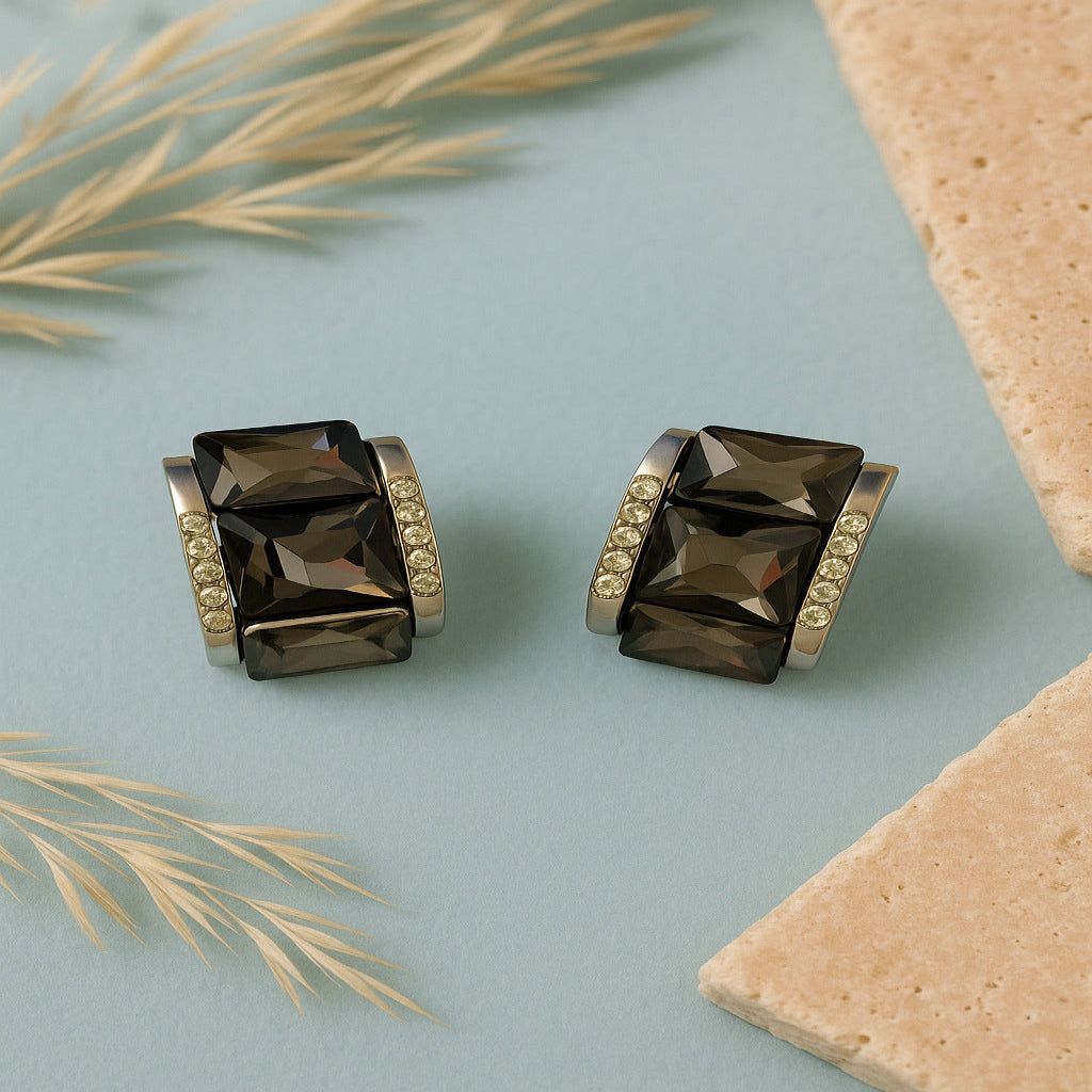 Pair of smoky quartz earrings with gold accents on a light blue background with beige leaves.