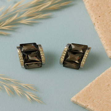 Pair of smoky quartz earrings with gold accents on a light blue background with beige leaves.