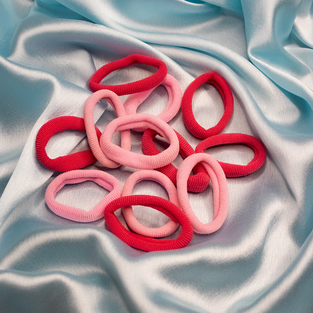 A collection of red and pink rubber bands arranged on a blue silky surface.