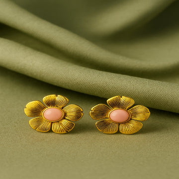 Gold flower-shaped earrings with a pink center on a green fabric background