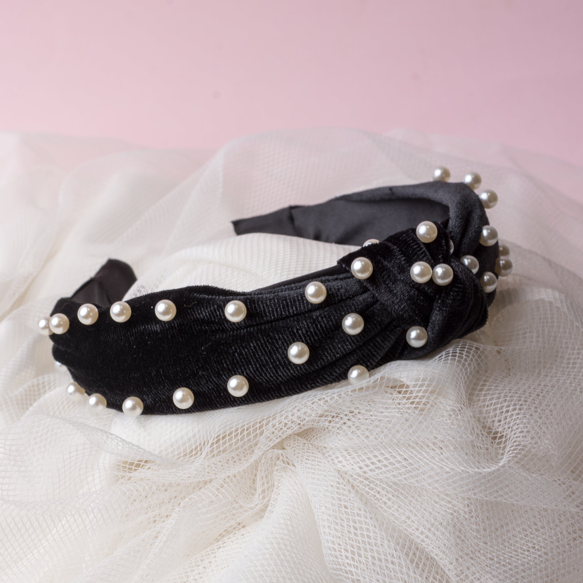 A black velvet headband with white pearl embellishments on a white fabric background.