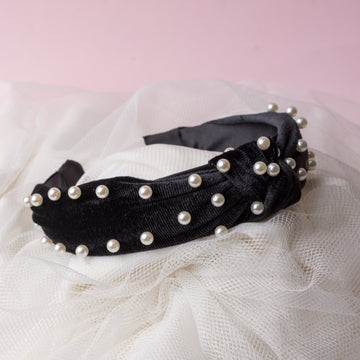 A black velvet headband with white pearl embellishments on a white fabric background.