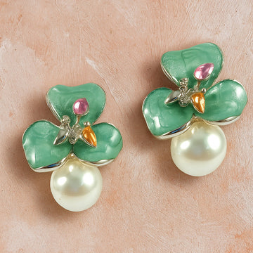 Green flower-shaped earrings with pearl drops on a beige surface