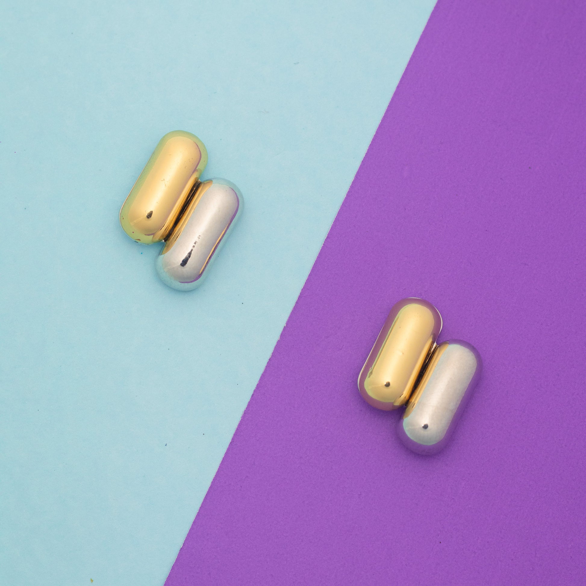 Two pairs of gold and silver earrings on a two-tone blue and purple background