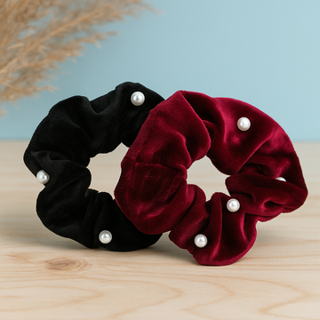 Black and red velvet scrunchies with pearls on a wooden surface and light blue background