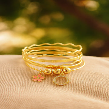 Set of gold bracelets with charms on a beige surface with a blurred natural background