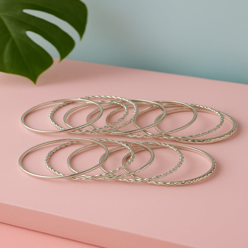 Set of silver bangles on a pink surface with a green leaf in the background