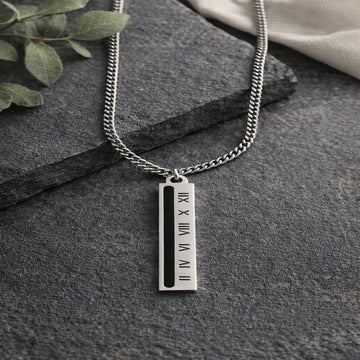 Silver mens  necklace with a vertical tag on a dark stone surface